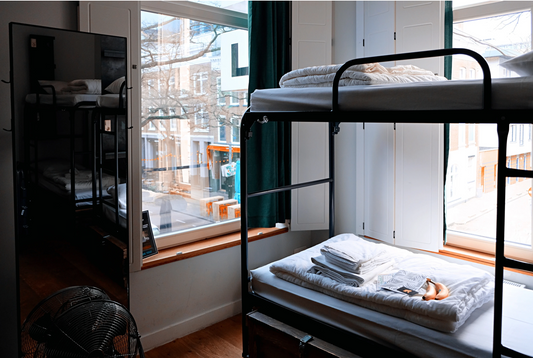 Bunk beds in the corner of a hostel dormitory with folded sheets and bananas on the bottom bunk